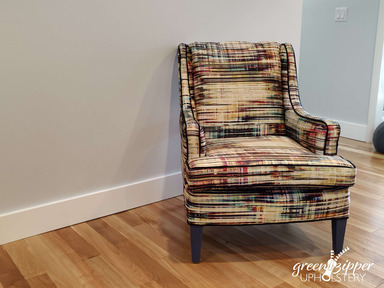 An upholstered armchair with a chenille graphic stripe pattern in multiple colors in front of a gray wall on a wood floor.