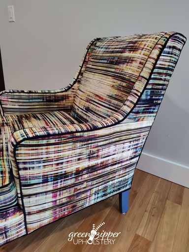 A reupholstered armchair with a graphic stripe pattern in multiple colors in living room in front of a gray wall on a wood floor.