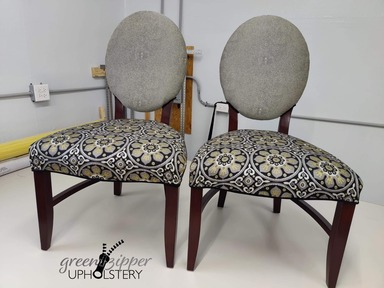 A front view of 2 dining room chairs with 3 fabrics in gray, black, white and gold patterns.
