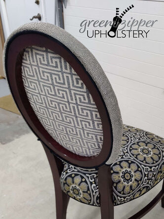 A back view of a dining room chair with 3 fabrics in gray, black, white and gold patterns.