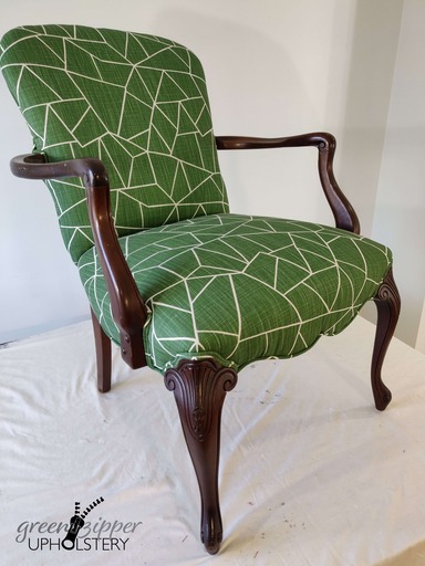 A chair with modern green and white fabric and wood arms and legs, on a work table with pale green wall.
