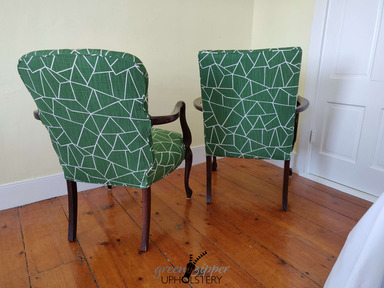 2 chairs with modern green and white fabric, wood arms and legs, in a room with yellow walls, white trim and door, on a wood floor.