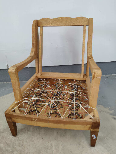 The wooden frame of a chair stripped down in preparation for reupholstery, with tied springs and webbing.