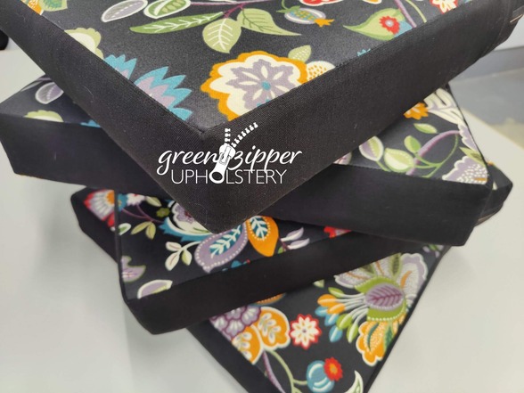 4 outdoor chair cushions stacked in a pile. The vibrant black floral fabric has solid black edge bands.