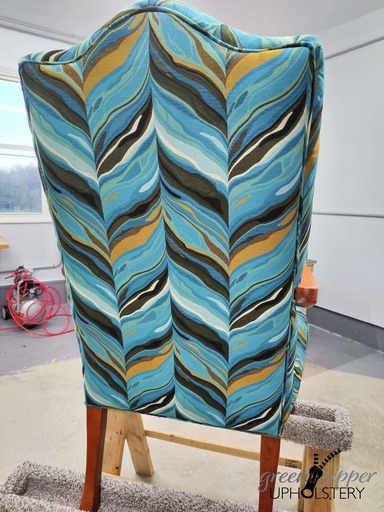 Back view of a vibrant chair with a modern pattern of teals, browns, and white, on a work table in a workshop.