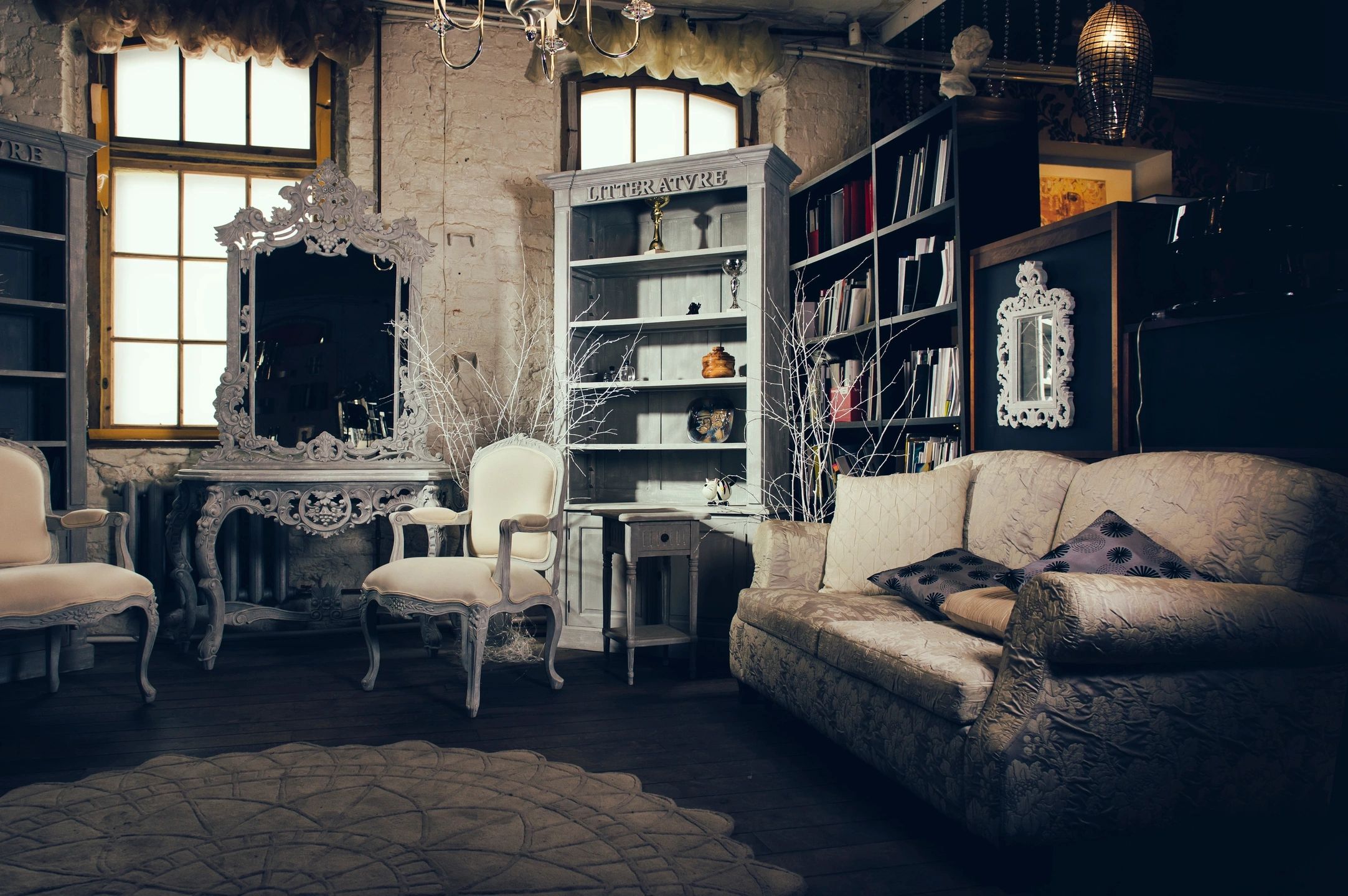 A photo of a room filled with antique bookshelves and wood furniture, a white antique armchair, and an upholstered couch.